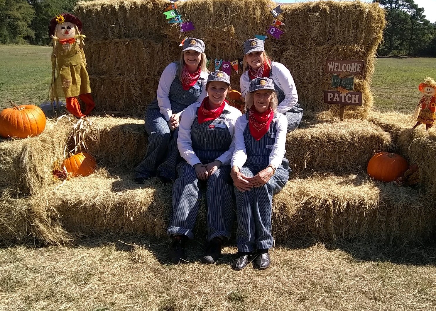 hay stacked 4 people sitting on the hay with railroad overalls, red bandanas and billed caps-several pumpkins and scarecrows